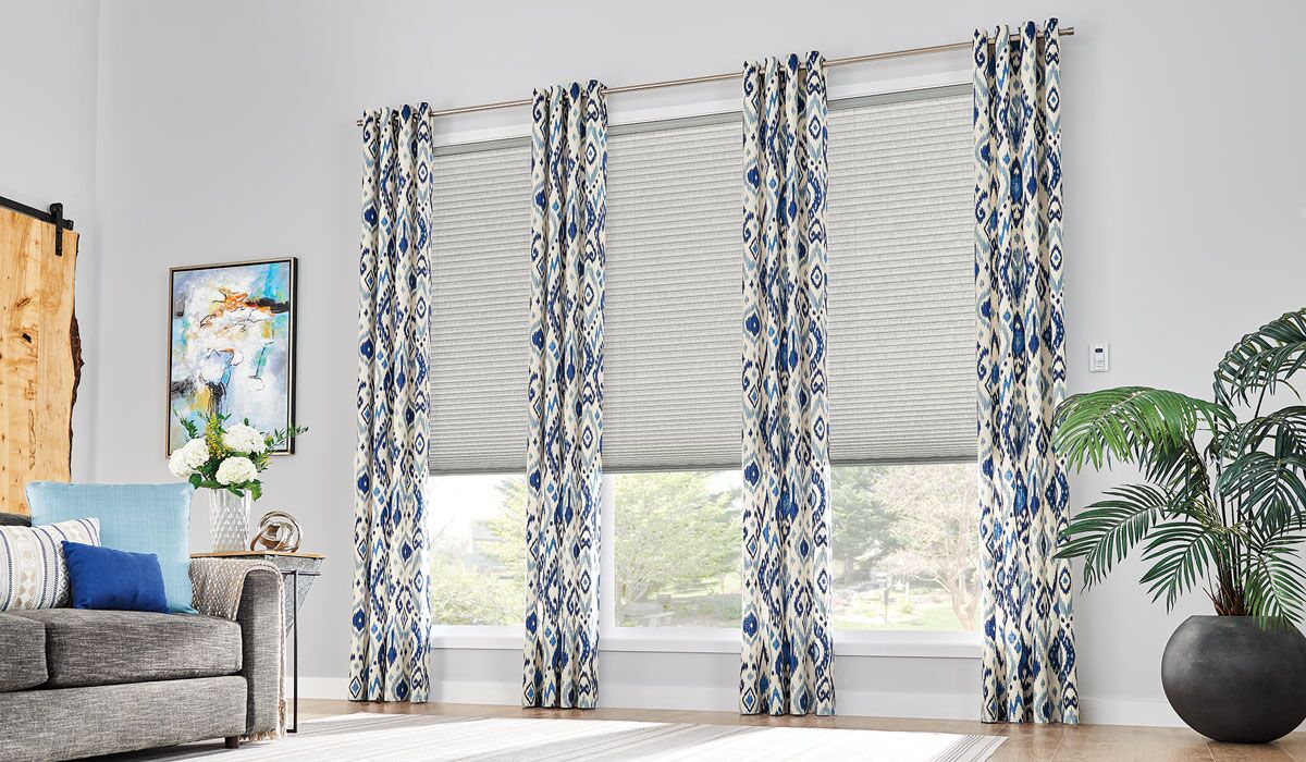 photo of a modern living room with light grey cellular shades layered with blue and white batik pattern curtains